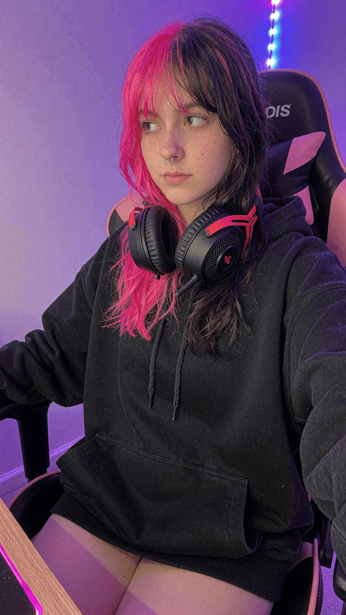 Woman with pink and black split-dye hair wearing gaming headphones under purple lighting